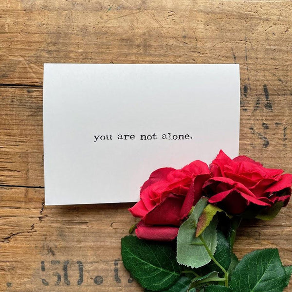 you are not alone greeting card in typewriter font with envelope and rose sticker.